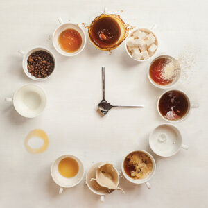 two spoons positioned like clock hands in the middle of a circle made of mugs with various coffee types