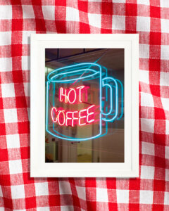 a neon sign in a window showing a blue mug with the words "hot coffee" in red