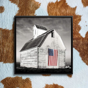 Black and white photo of a white barn with an American flag on the front door