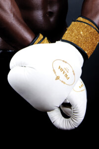 Photo of a black man with crossed arms wearing white boxing gloves with gold trim and a Prada logo