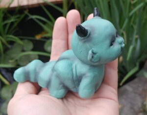 Teal colored figurine of baby demon grub with horns