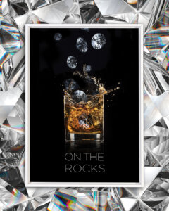 Photo of a rocks glass with scotch in it and diamonds falling into it on a black background with text that says "On the rocks"