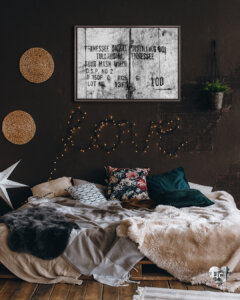 Rustic wood engraving-inspired graphic of Tennessee whiskey distilling label framed on a brown wall in a bedroom with string lights and a potted plant
