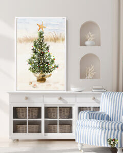 Print of a Christmas tree on a beach leaning on a white dresser in a coastal room with a blue and white arm chair