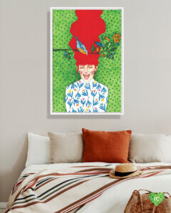 Image of a woman with red flowing hair yelling with eyes closed on a green background next to a tree branch with a bird on it, framed in white in a bedroom with an orange throw pillow