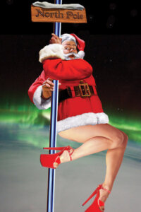 Santa with female legs and high heels swinging around a stripper pole with a sign that says North Pole