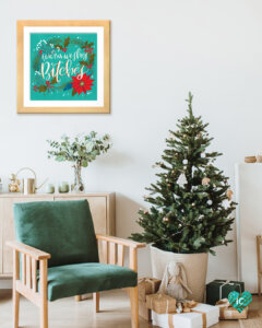 Typography print with holiday elements that says "Warm Wishes Bitches" in a frame on a wall in a room with a mini Christmas tree and a green chair
