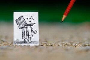 “Pencil vs. Camera - 38” by Ben Heine shows a pencil drawn robot on a piece of paper with a red pencil in view.