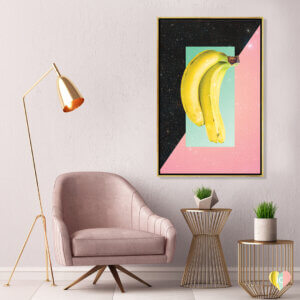 Two bananas over a pink and black sparkly background framed in gold hanging on a wall in a room with gold and pink deco style furniture
