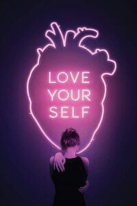 Graphic of a pink neon outline of a human heart with text inside that says "Love Your Self" with a female standing in front of it as she hugs herself