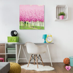 Image of a cluster of pink trees in a green field hanging on a wall in a kid's room with a desk, plant, and basketball