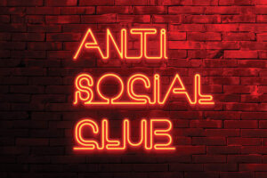 Image of a red brick wall with a neon text sign in red letters that says "Anti Social Club"