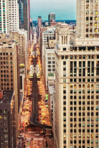 “City View” by Bill Carson Photography shows an aerial view of a busy city street surrounded by towering skyscrapers with a train line seen above the road.