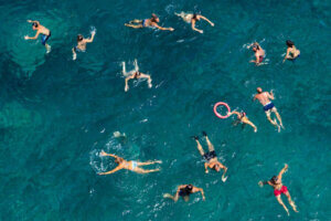 “Untitled” by Carlo Tonti shows an overhead view of people swimming in a body of water.
