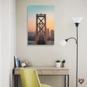 “Bay Bridge San Fran” by Peter Yan shows the San Francisco Oakland Bay Bridge against an ombre blue and yellow sky with buildings in the distance.