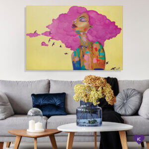 Painting of the profile of a black woman with pink hair and splashes of paint on her body with small pink birds flying around her against a yellow background, on a wall over a living room couch