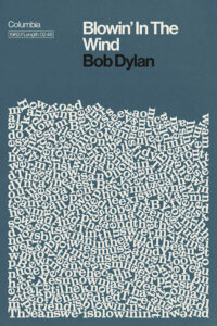 “Blowin In The Wind By Bob Dylan Lyrics Print” by Reign & Hail shows the lyrics to the song “Blowin In The Wind” by Bob Dylan jumbled in a pile against a blue background.
