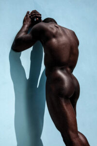 "Blue Nude" by Gregory Prescott shows a photo of the backside of a black man leaning up against a blue wall