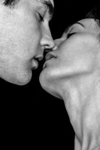 "Kiss" by Gregory Prescott shows a black and white photo of the profiles of a man and a woman about to kiss