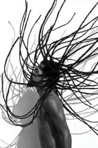 "Locs" by Gregory Prescott shows a black and white photo of the profile of a man with long dreads in the air