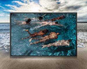 "Swim Meet" by Gregory Prescott shows a photo of seven people of various genders and races swimming in blue water