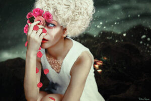“Forlorn” by Victoria Obscure shows a woman with bleached hair holding pink roses over her glowing blue eyes.