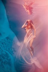 Surreal Dreams by Lola Mitchell showcases a nude woman floating under pink and blue water while wrapped in sheer fabric
