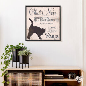 Framed wall art of black cat by iCanvas artist Color Bakery above a tan table with green plants