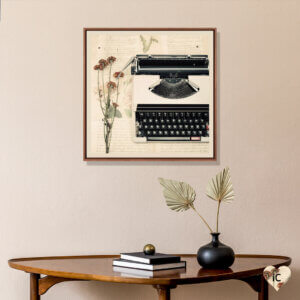 Framed wall art of a typewriter and flowers by iCanvas artist Caroline Mint above a table with books and fronds
