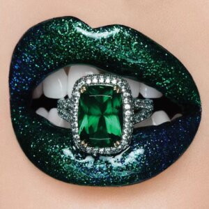 Green sparkling lips and teeth biting an emerald diamond