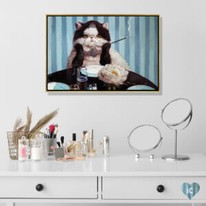Framed wall art by Lucia Heffernan of a cat styled like Aubrey Hepburn in Breakfast At Tiffany's above a makeup vanity