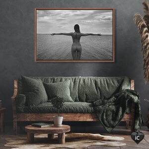 Green couch below black and white framed photo of the back of a naked woman looking at a body of water with her arms spread