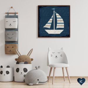 Framed art of a white sailboat with gray, white and blue striped sails against blue background mounted above child’s toys