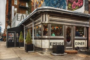 Wall art of a corner diner below a city mural demonstrating the authenticity trend by iCanvas artist Alison Frank