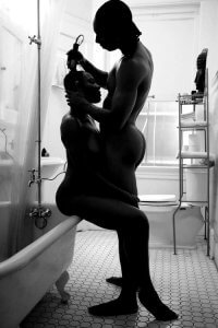Black and white photograph of a naked man giving a naked woman a haircut as she sits on the tub by Gregory Prescott
