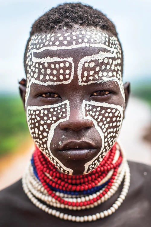 Photographed portrait of a Black man wearing beaded necklaces with white paint and dots on his face