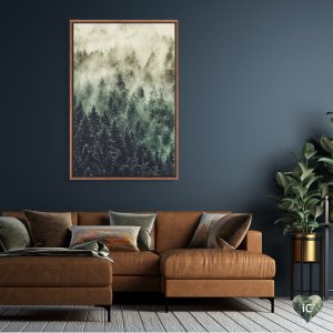 Framed nature photograph of green pines beneath fog by Tordis Kayma mounted above brown couch