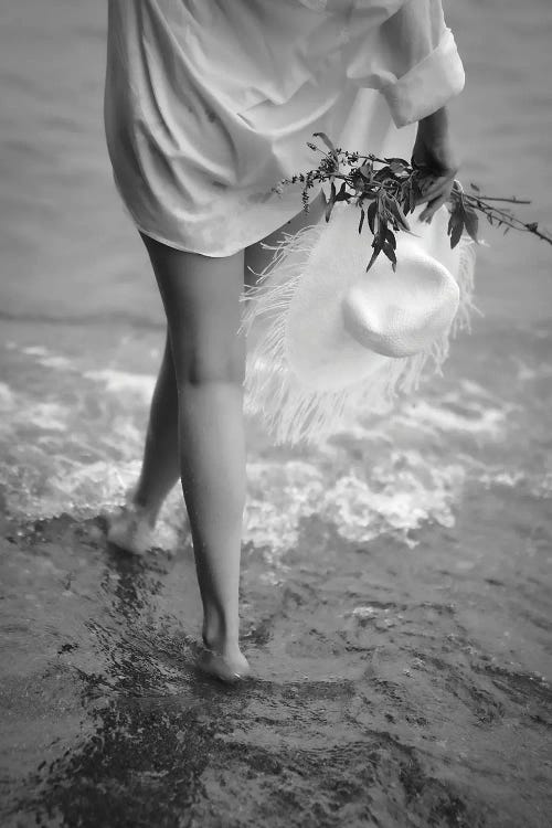 Black and white photograph of a woman’s legs as she walks in water carrying flowers and a hat by new creator Teal Production