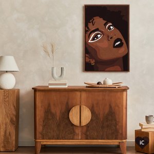 Framed wall art of Black woman portrait with white eyeliner and black lipstick above cabinet by Phung Banh