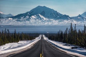 Open road surrounded by snow leading to large mountains.