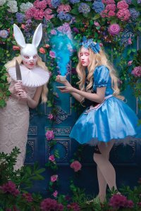 A picture of a depiction of Alice from Alice in Wonderland holding a cup of steaming tea next to a woman wearing white rabbit ears and holding a knife.