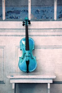 A blue violin on an old white bench leaning against a distressed white wall.