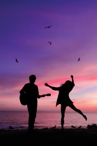 Silhouette of man and woman with guitar in front of pink and purple sunset