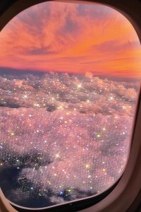 Glittery clouds outside of airplane window with orange sunset