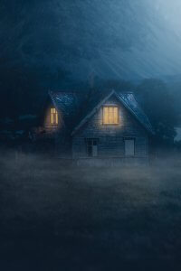 Nighttime house with lit windows surrounded by fog